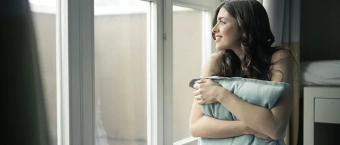 Woman sitting by a window holding a cushion