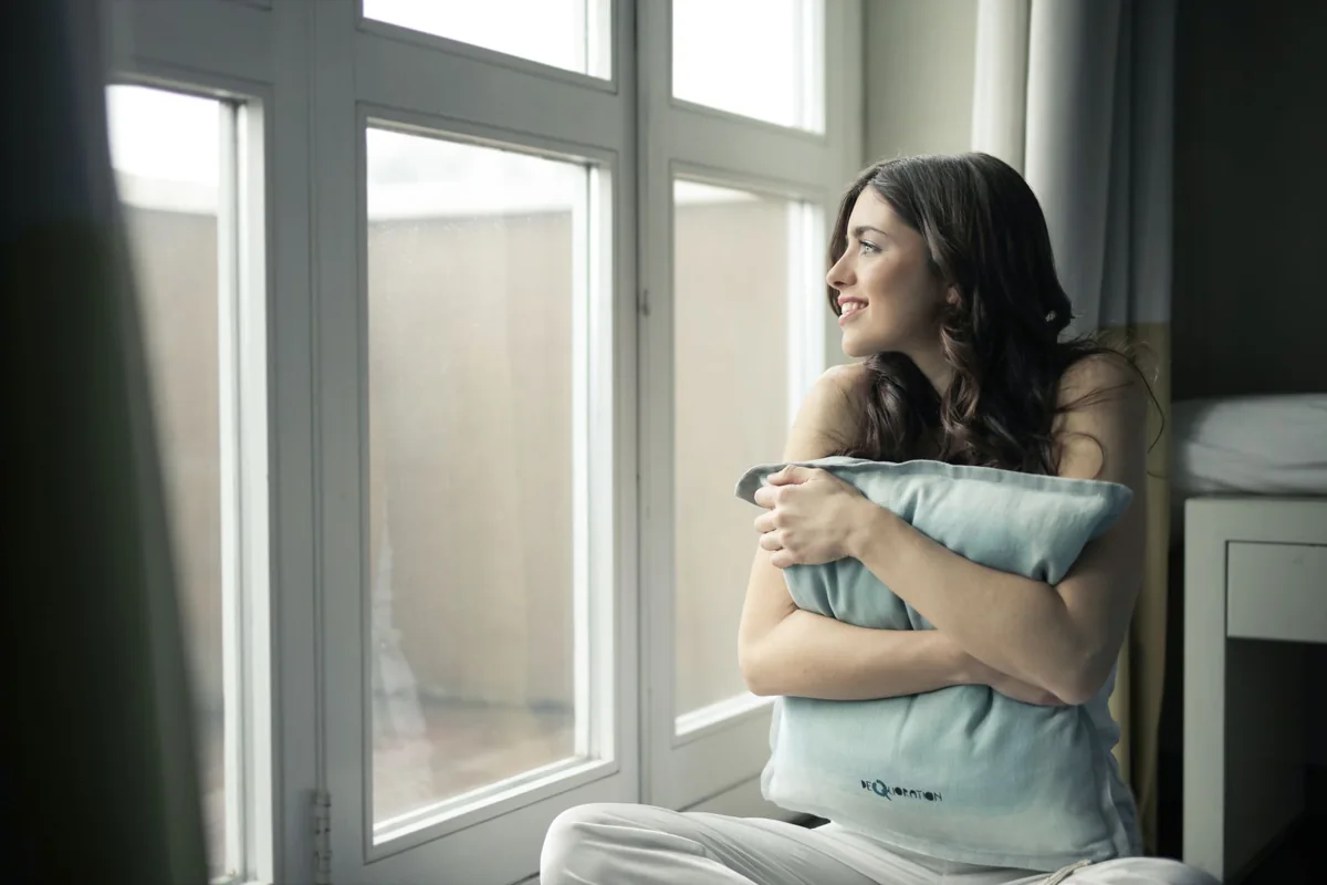 Woman sitting by a window holding a cushion