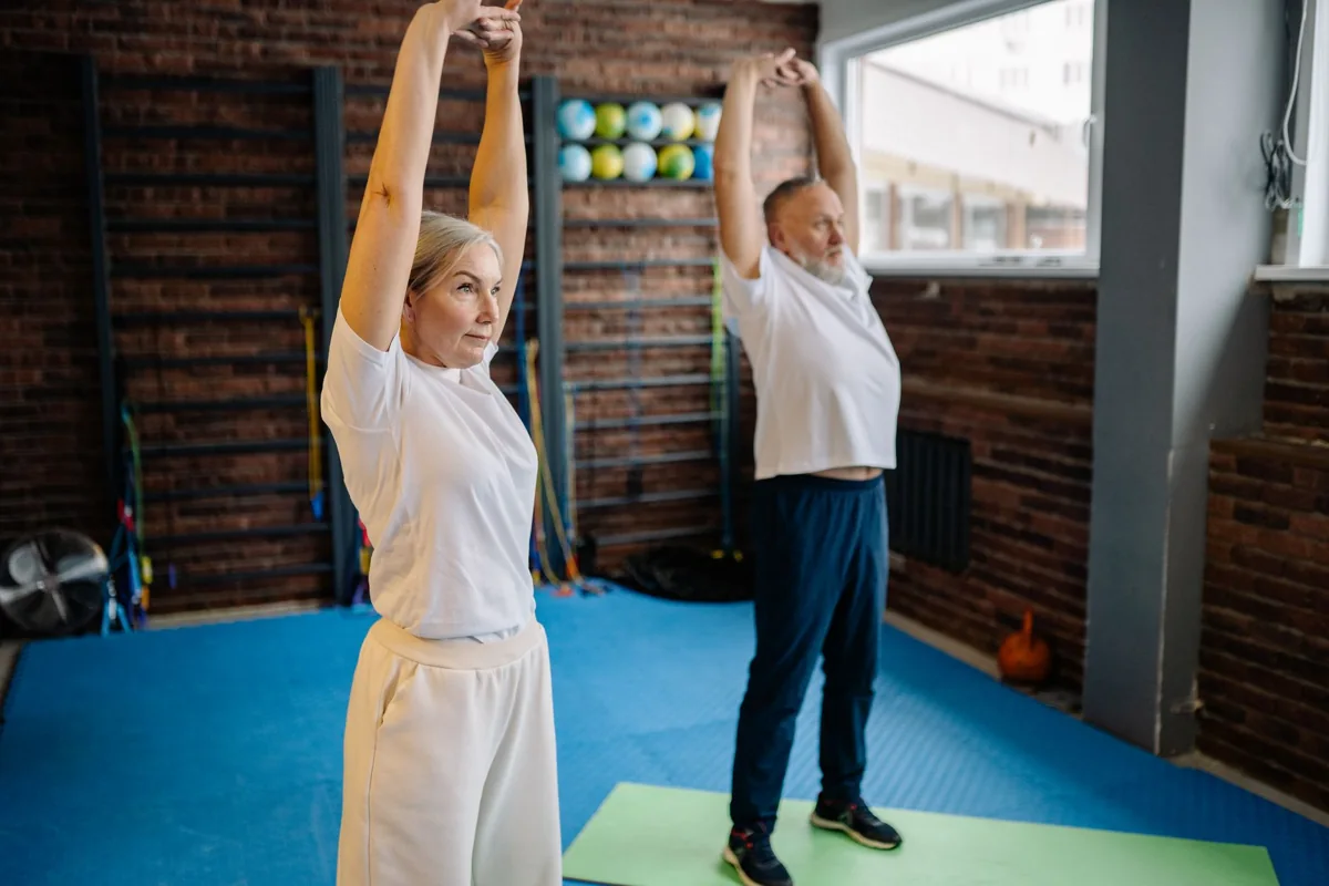 Two adults raising their arms while stretching indoors