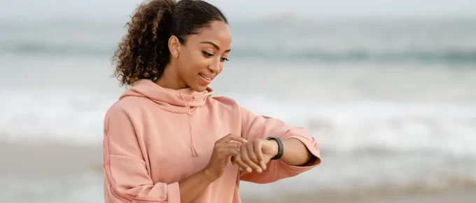 Woman in a pink hoodie checking her smartwatch on a beach