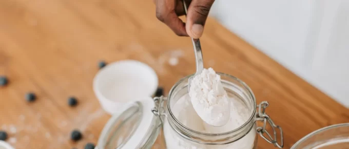 Spoon lifting protein powder from a glass jar on a wooden table