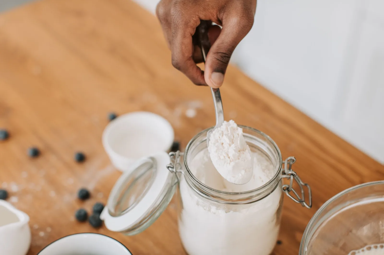 Spoon lifting protein powder from a glass jar on a wooden table