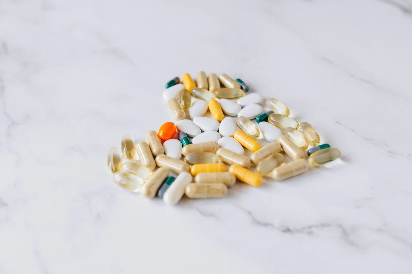Mixed vitamin capsules and tablets arranged on a marble surface