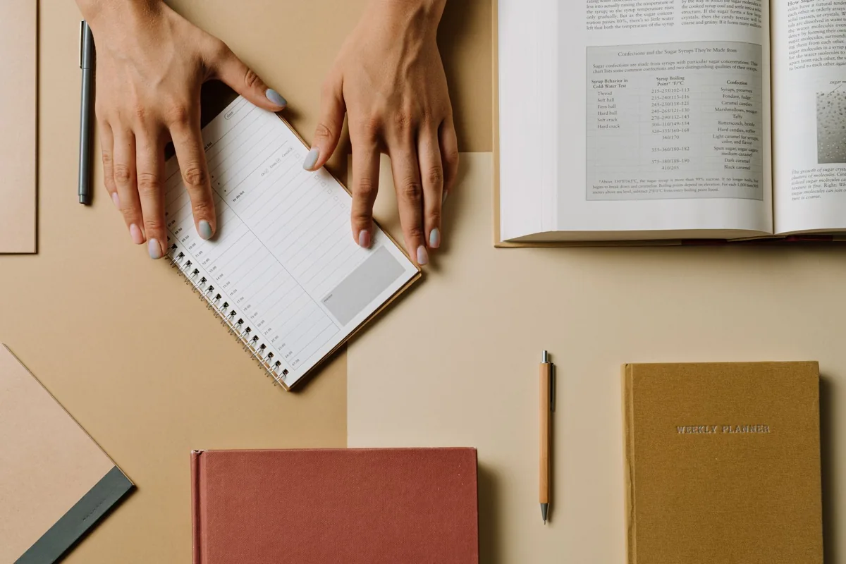 Hands writing in a notebook beside a book